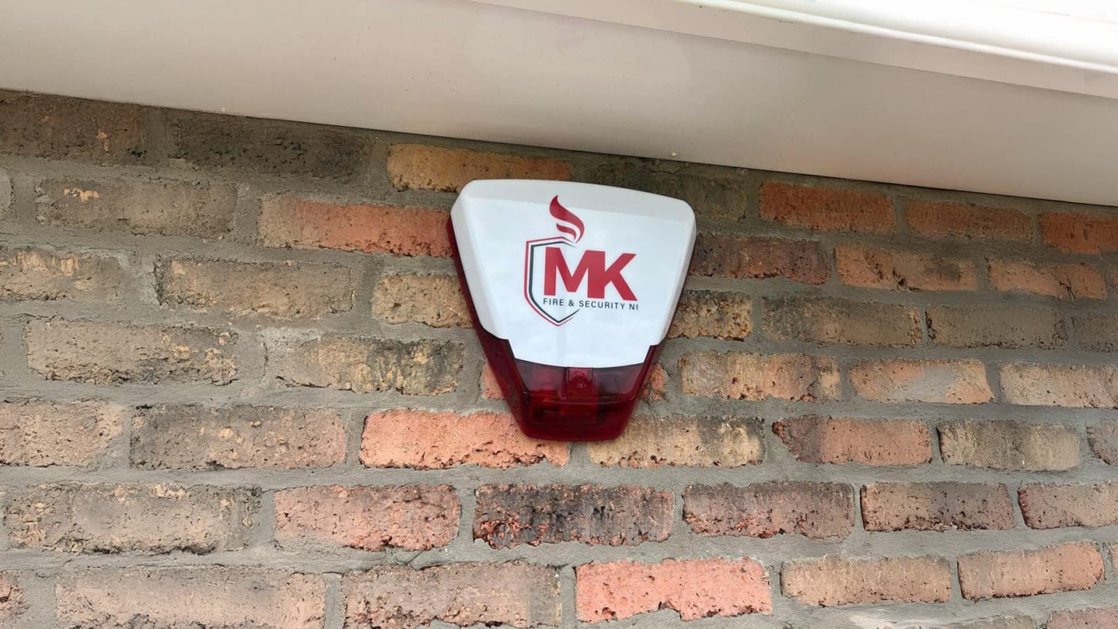 MK Fire & Security NI branded external alarm sounder installed on a brick wall