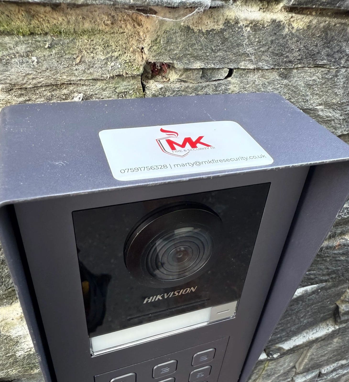 Door entry station with a keypad and camera fitted beside a stone-faced entrance